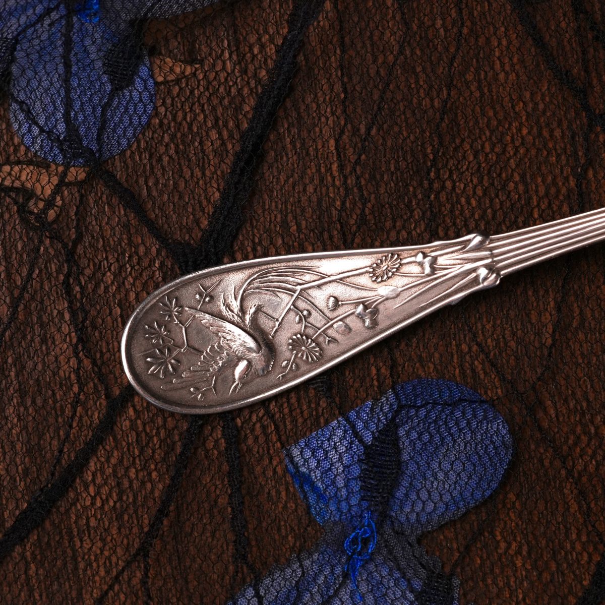 Close detail of the Tiffany Japanese pattern handle — a long-legged wading bird cast in relief among star-shaped blossoms, grasses and a chrysanthemum, composed asymmetrically